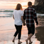 MEDIUM IMAGES (20) Young couple holding hands, walking on a beach at sunset.